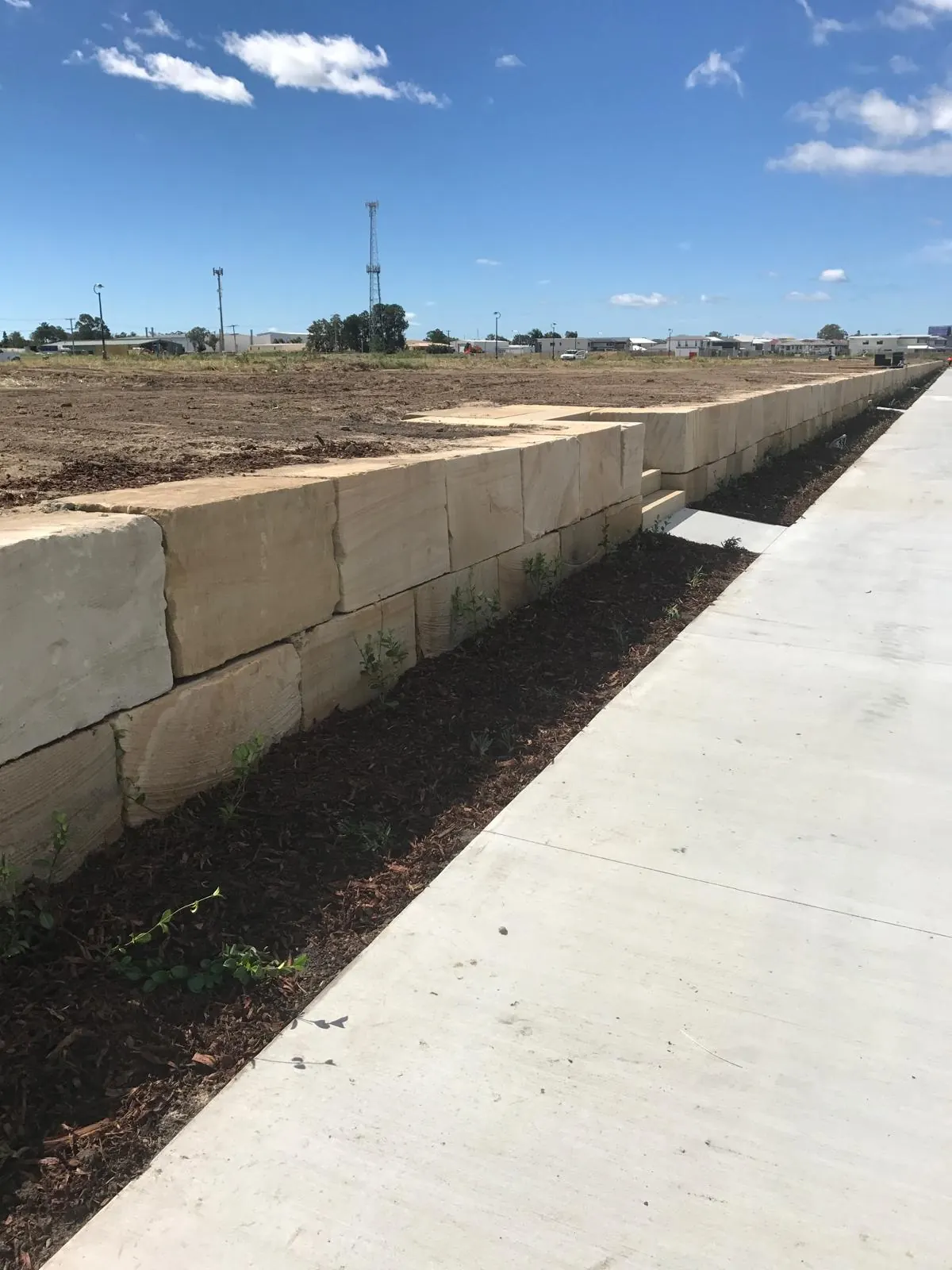 Long sandstone wall beside a new concrete path